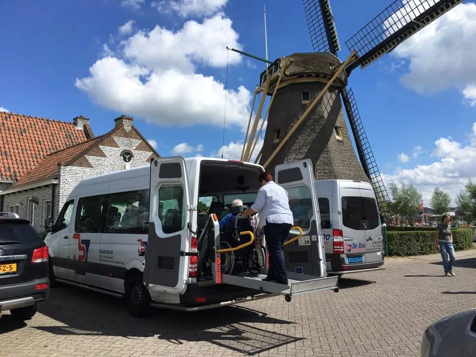 Een reiziger wordt met de lift in een aangepaste De Roo-bus geholpen